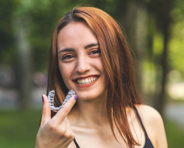 smiling woman holding Invisalign and learning about the cost of Invisalign in West Seneca