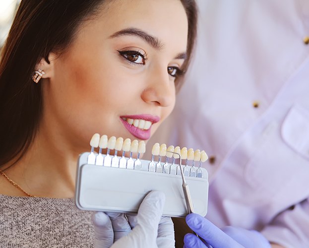 Woman smiling while cosmetic dentist holds veneer color chart
