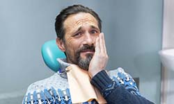 Man in dental chair holding his cheek in pain