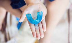 Outstretched hand holding mouthguard to prevent dental emergencies in West Seneca