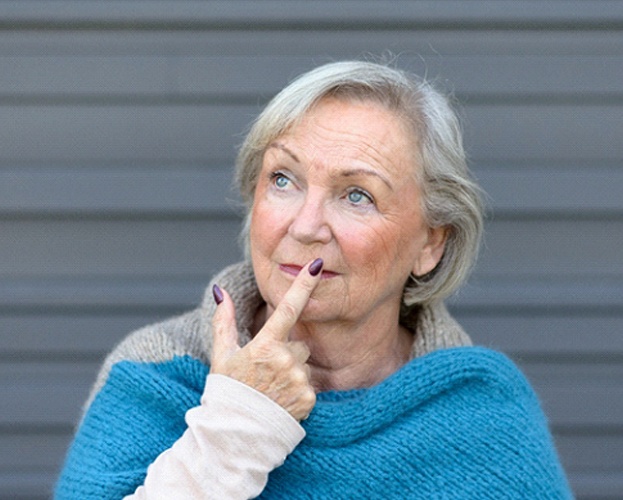 older woman thinking about the symptoms of dental implant failure in West Seneca