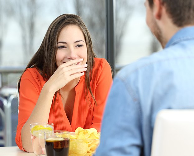 Woman in need of gum contouring hiding her smile while talking