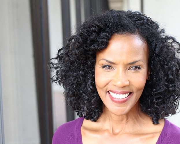 woman with curly hair smiling after working with an implant dentist in West Seneca