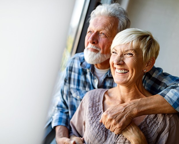 older couple smiling and hugging while looking out of a window