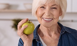 woman with dental implants in West Seneca holding an apple