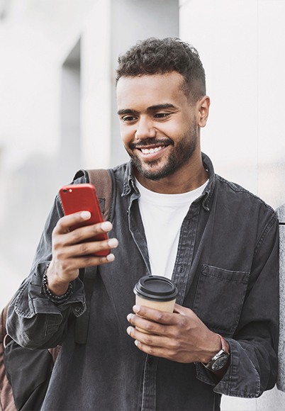 Man smiling at his cell phone while holding coffee cup
