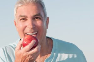 man eating an apple and making the transition to implant dentures